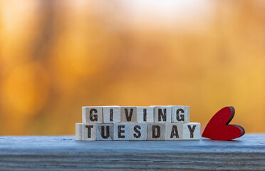 Giving Tuesday text on wood blocks with red heart golden leaves bokeh background