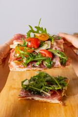 Pensa romana con prosciutto crudo, pomodori, scaglie di formaggio e rucola mentre viene tenuta tra le mani di una cliente di una rosticceria