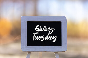 Giving Tuesday text message on chalkboard easel soft bokeh background copy space