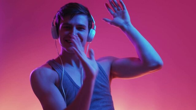 Dancing man. Neon light portrait. Stereo sound. Happy funny guy in headphones moving on music on blue purple background slow motion.