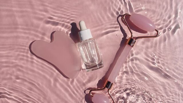 Cosmetic bottle with pipette and Massage roller on water with drops on a pink background. Pure water with reflections sunlight and shadows. Video of packaging for advertising, products High quality 4K