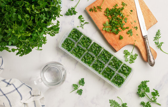 Frozen herbs for cooking. Fresh organic parsley and parsley ice cubes on a marble background. The concept of frozen food. Selective focus, top view and copy space