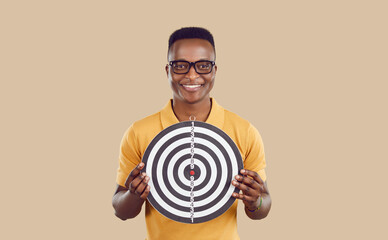 Young happy African American man holds dartboard in front of him symbolizing desire to achieve...