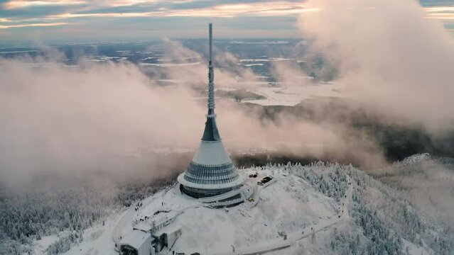 Jested tower built on high forestry mountain top covered with snow. High construction with futuristic design and sharp spire in haze aerial view