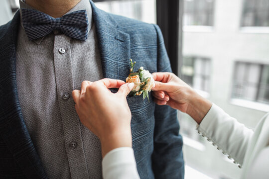 The bride attaches a boutonniere to a stylish groom
