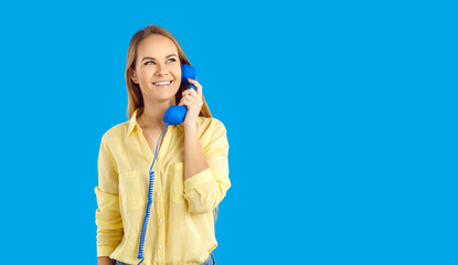 Smiling young woman on blue studio background talk on landline telephone. Happy millennial girl have pleasant call with customer service on corded phone. Helpline support. Copy space. - obrazy, fototapety, plakaty