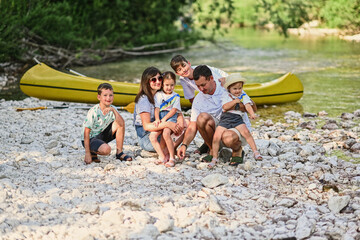 Obraz premium Family with four kids against canoe in rocky shore of a calm river in Triglav National Park, Slovenia.