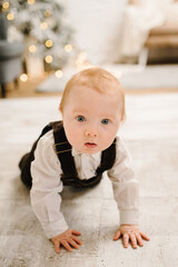 Naklejka premium Little smiling and surprised baby boy crawling near Christmas tree. Christmas gifts, presents for New Year. Child looking magic boxes at home. Beautiful living room interior with winter decor. Closeup
