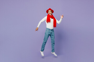 Full body side view happy smiling young middle eastern man he wear white turtleneck red hat scarf point index finger aside on workspace area jump high isolated on plain pastel light purple background.