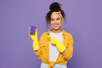 Young happy housekeeper woman wear yellow shirt rubber gloves hold point index finger on violet...