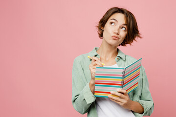 Young woman 20s wear green shirt white t-shirt writing down in notebook diary remind memories and make list of dreams isolated on plain pastel light pink background studio People lifestyle concept.