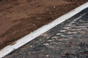 Asphalt texture with a white line that separates the asphalt from the freshly carved flower bed with brown sand.