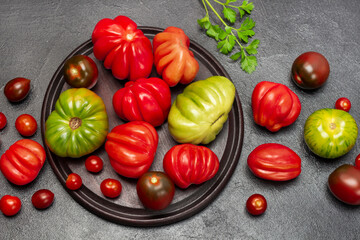 Fototapeta na wymiar Green, red and brown tomatoes on board and table. Sprig of parsley.