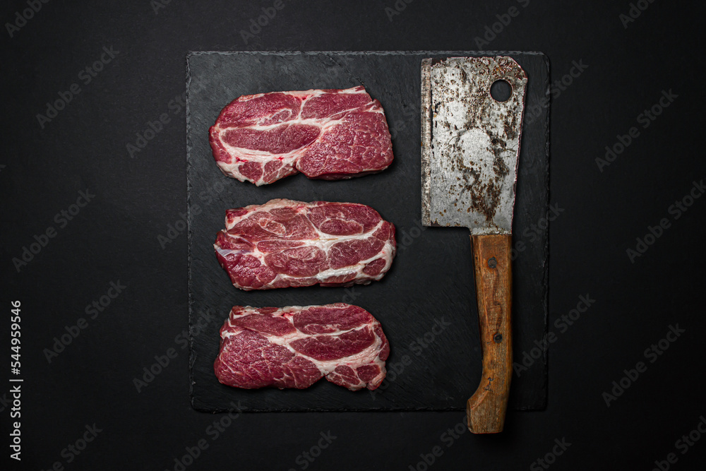 Canvas Prints A slice of raw fresh meat with a kitchen hatchet on a black background.