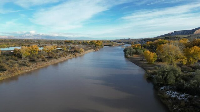 Aerial of Colorado River in Grand Junction lined with yellow aspen trees in fall with the Colorado National Monument in background