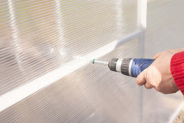 a man's hand twists a screwdriver in the greenhouse