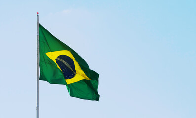 Brazilian flag waving in a beautiful clear sky, with the sunlight lighting up the flag. Brazil flag on the left with space for text on the right.