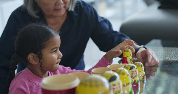 Senior woman assisting granddaughter playing with nested dolls