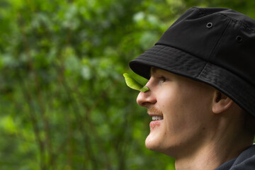 Portrait of smiling young man in black panama hat with green maple spout, maple seeds on his nose, side view. - Powered by Adobe