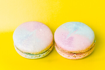 Tasty colorful macaroon. Two blue and pink macaroons on a yellow background. Most delicate cake is a cookie made of two smooth halves, fastened with fillings. French pastry made from egg whites.