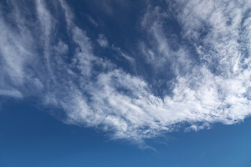 Picturesque cloudscape background with light spindrift clouds on a dark blue sky