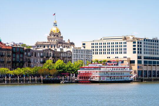 Savannah, USA - May 11, 2018: River street old town waterfront by Georgia Queen steamboat cruise ship, golden dome city hall and Hyatt regency hotel cityscape skyline