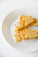 Juicy pieces of yellow cheese with holes on a white plate. Delicious slices of cheese close-up.