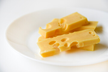 Juicy pieces of yellow cheese with holes on a white plate. Delicious slices of cheese close-up.