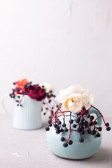 Postcard with fall roses and wild blue berries in blue jvase and teal napkin  on light background. Selective focus. Still life. Romantic postcard. Place for text.