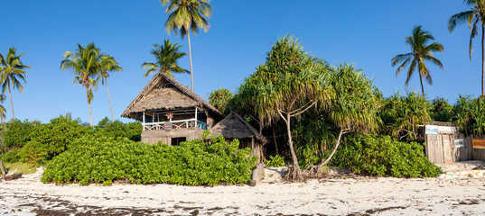 Fototapeta premium Sansibar, Matemwe Beach in Tansania. Holzhütten und Palmen an einem Strand an der Küste der karibischen Insel im Indischen Ozean von Afrika und blauer Himmel, Panorama.