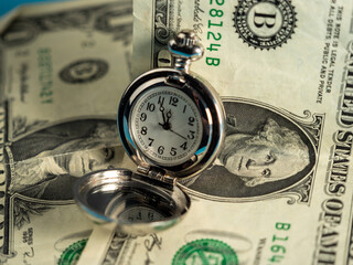 Old pocket watches lie on dollar bills.