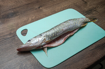 The cook cuts raw pike fish on a cutting board with a knife