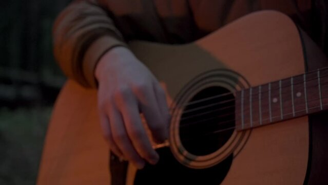man hand playing guitar outdoors in park. Strumming acoustic guitar close-up. musician in a forest next to a fire