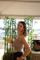 Young woman holding her cocktail and smiling. Bamboo background. 