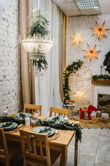 Christmas festive table with candles in living room. Interior with New Year's decor at home. House is decorated with ornaments tree branches, gifts boxes, garlands and toys. Concept of winter holiday.