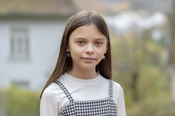 Street portrait of an 11-year-old beautiful and neat schoolgirl girl with long dark hair on a neutral blurred background.
