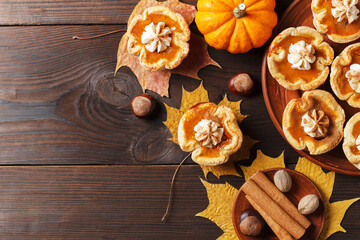 Pumpkin mini pies with whipped cream and spices on a wooden background. copy space