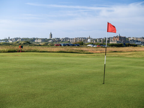 Red hole flag on golf course with urban skyline behind