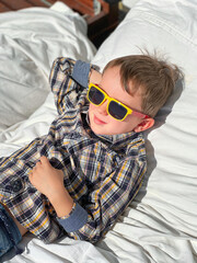 Cute boy wearing glasses relaxing on bed in patio