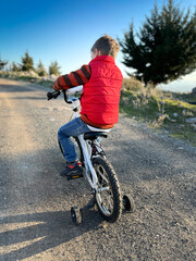 Rear view of boy in jacket riding bicycle on road