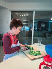 Boy cutting broccoli on board in kitchen