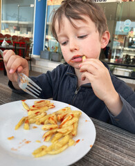 Cute boy eating french fries at restaurant