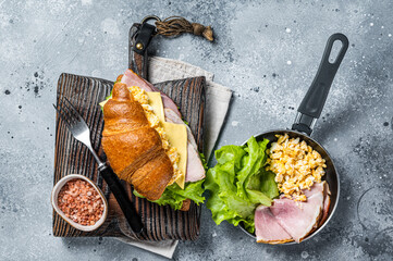 Croissant sandwich with turkey ham, scrambled eggs, cheese and lettuce salad. Gray background. Top...