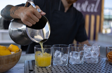 Young barman gently pours finished cocktail into glass. Barman's face is not seen in photo.