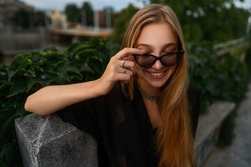 Cute blonde girl with sunglasses is smiling and having fun. Summer vibe picture. Natural portrait of a beautiful young laughing woman in the park.