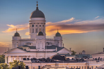 Fototapeta na wymiar Helsinki, Finland - July 19, 2022: Closeup of golden sunset over the white stone Cathedral with cityscape up front under yellow-gray cloudscape