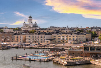 Helsinki, Finland - July 20, 2022: The white Cathedral with green domes towers over the port, the public swimming pool, Atlas Restaurant and cityscape under blue sunset cloudscape