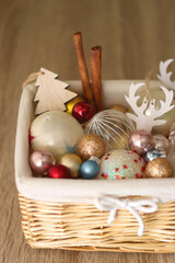 Wicker basket filled with various colorful Christmas decorations on wooden table. Selective focus.