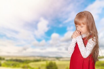 Happy young child praying on big field background.