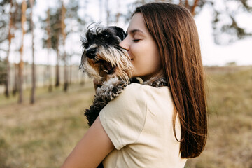 Young brunette woman hugging a miniature schnauzer breed dog, kissing it.